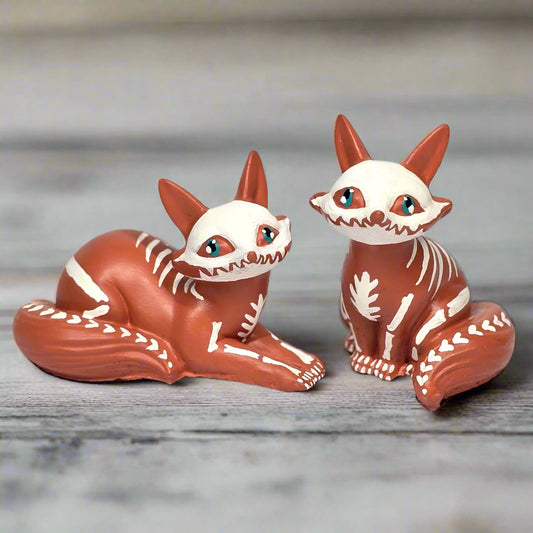 Two fox figurines with white faces on a light gray background
